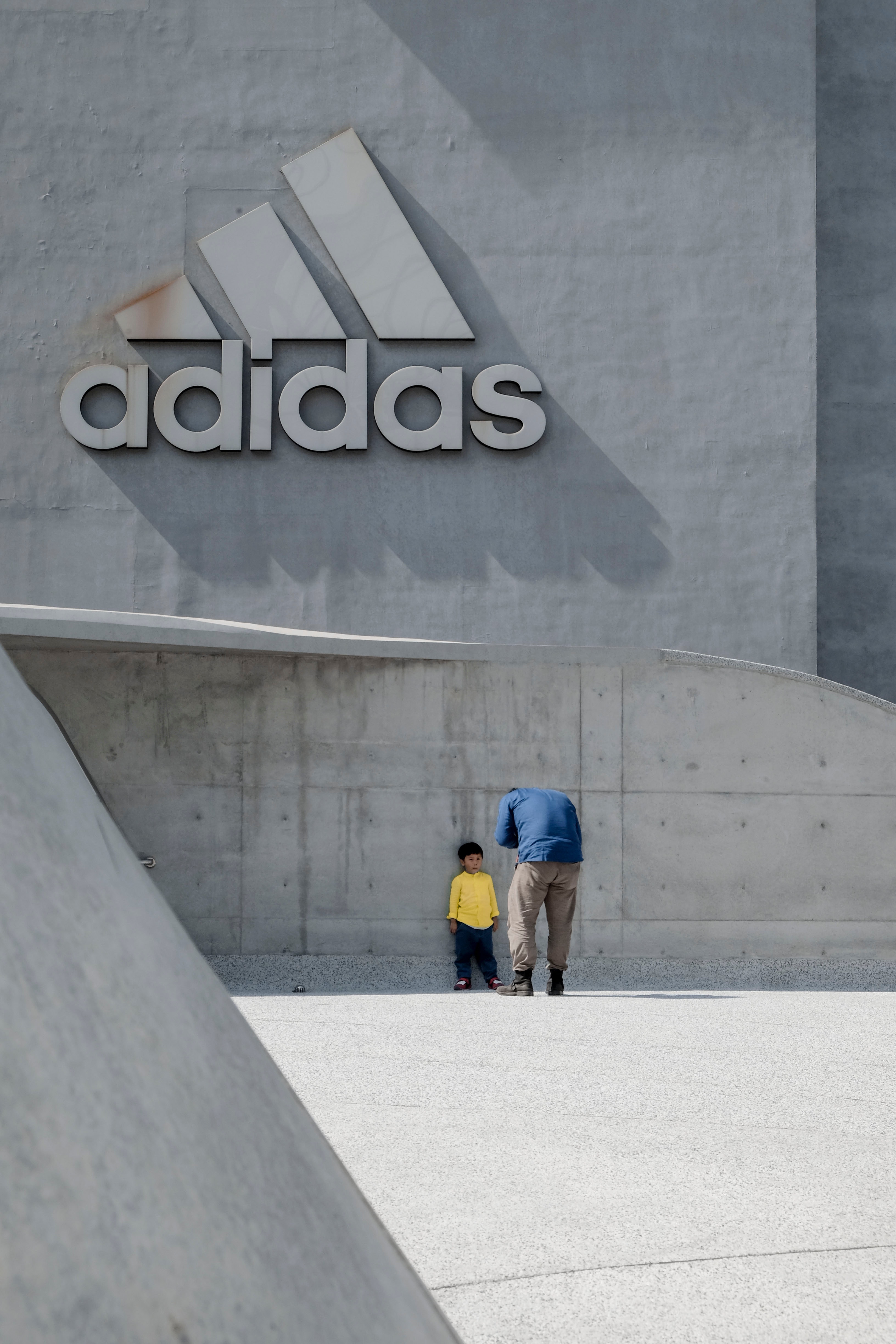 man and boy against a grey wall with Adidas on it.