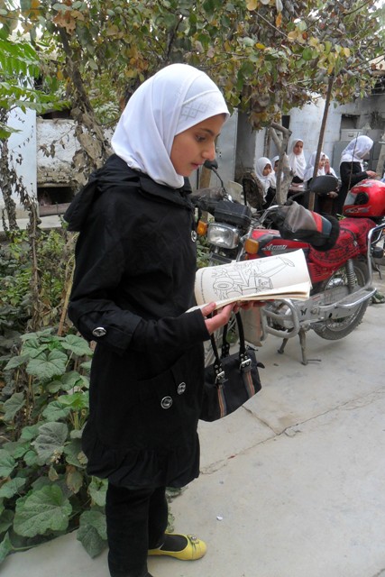 Women in Afghanistan reads a book on sidewalk